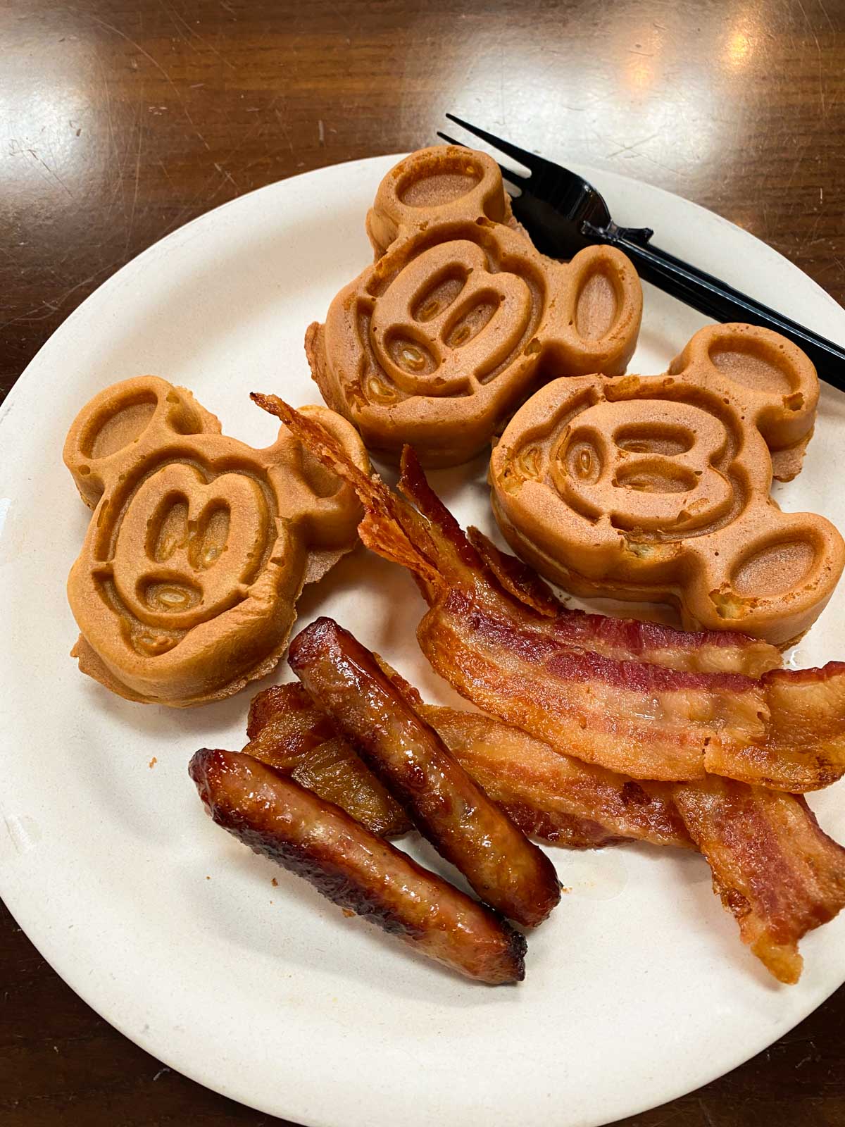A breakfast platter with Mickey-shaped waffles and breakfast sausage and bacon.
