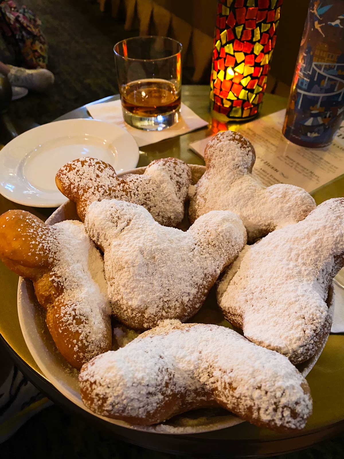 A platter of powdered sugar covered mickey-shaped beignets sits on a cocktail table.