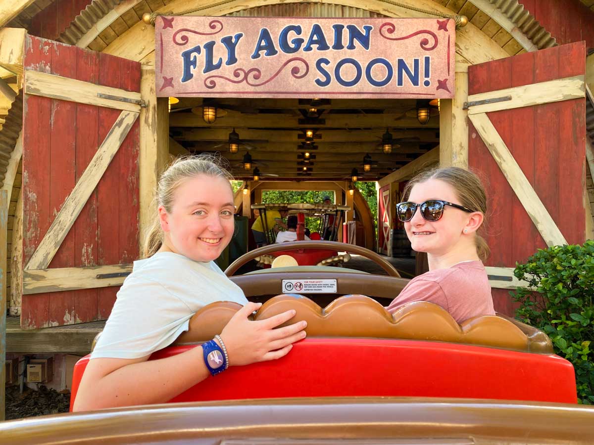 Two girls smile at the end of the ride with a sign that says "Fly again soon!"