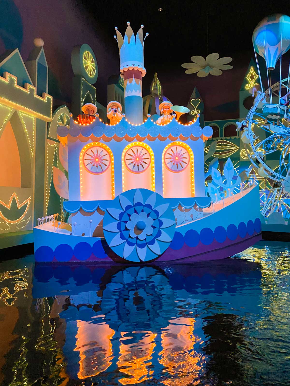 A scene from inside the ride shows a boat all lit up with dancing dolls on top.