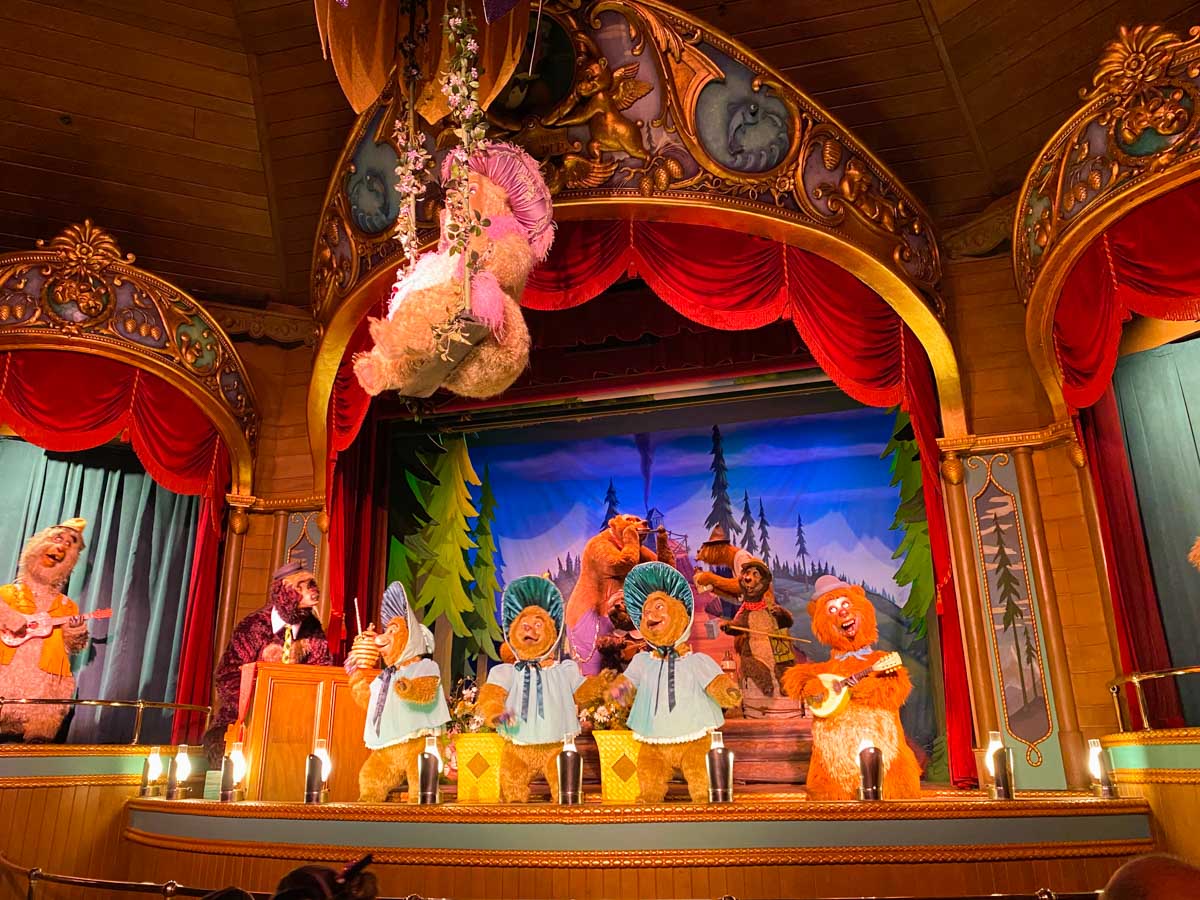 Animatronic bears singing on a stage with a red velvet curtain.
