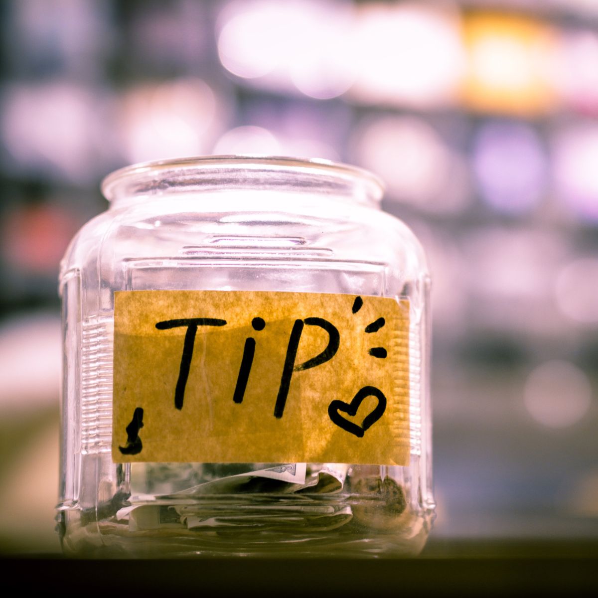 A tip jar has some money insie and a label with a heart.