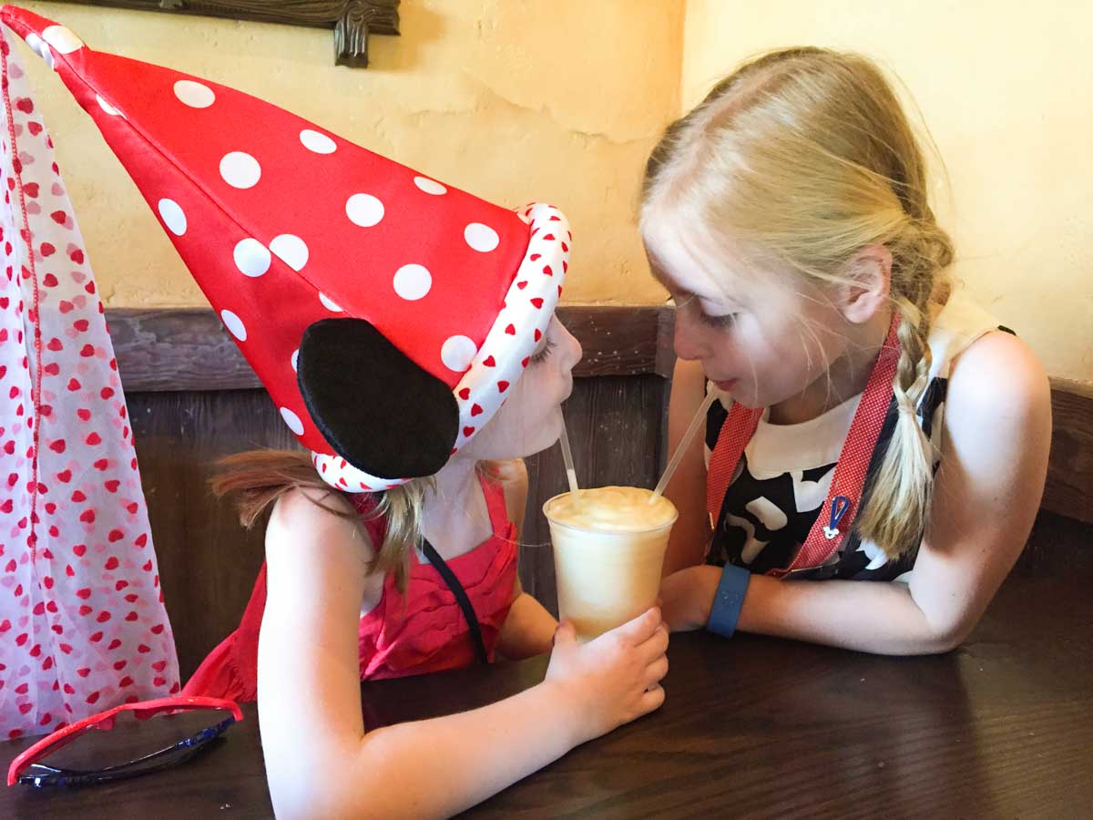 Two girls share a drink at Gaston's Tavern. One is wearing a red and white polka dot hat.