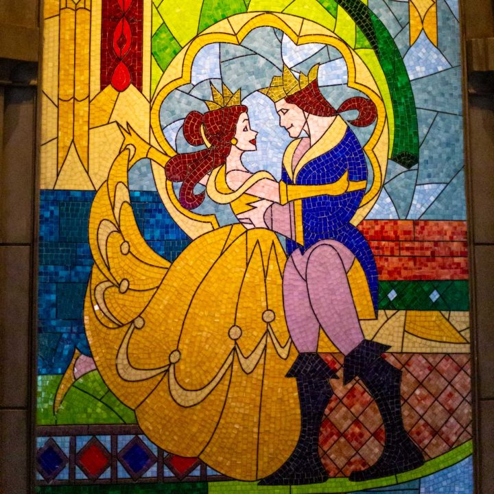 A stained glass window portrays Belle in her yellow dress and the beast as a prince.
