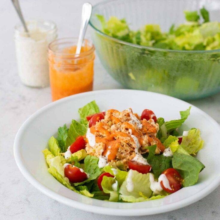 A plate of lettuce with tomatoes and buffalo chicken.