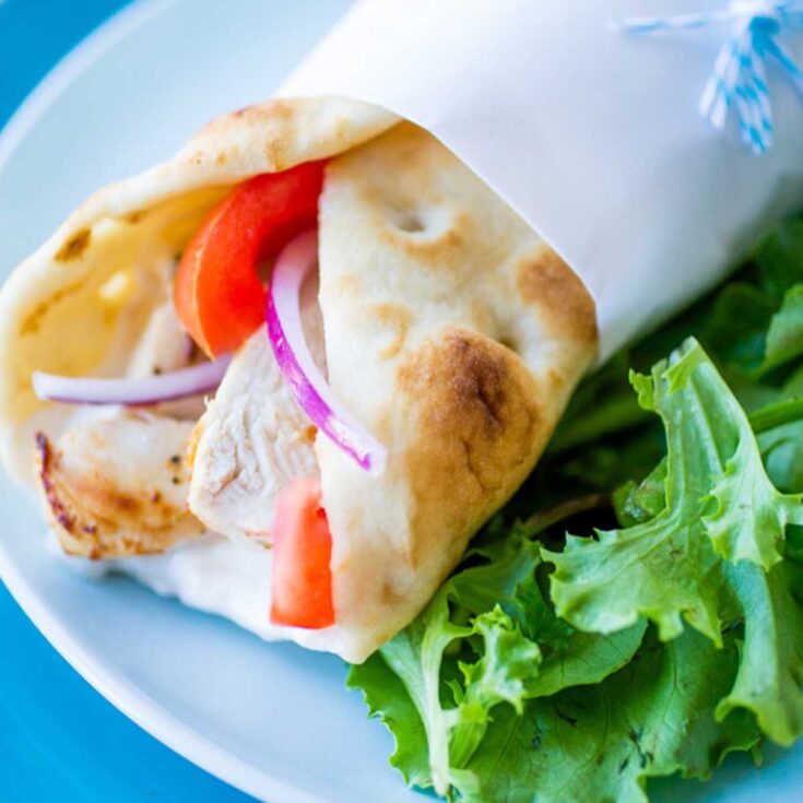 A pita has chicken, tomato, and red onion peeking out. Lettuce is on the side.