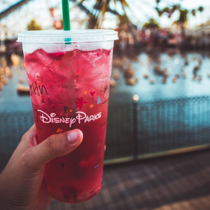 A hand holds an icy beverage with a straw that says "Disney Parks."