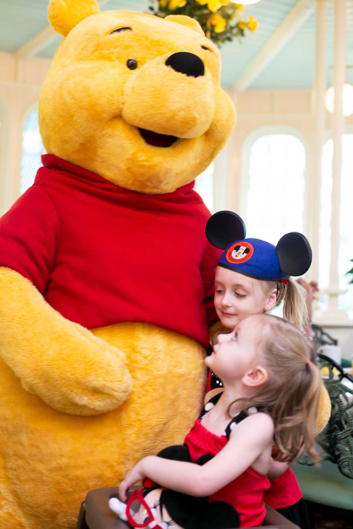 Winnie hugs two young girls wearing Mickey Mouse ear hats.