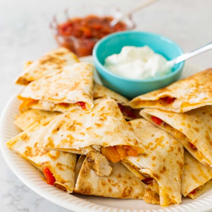A plate of jerk chicken quesadillas with sour cream and salsa.