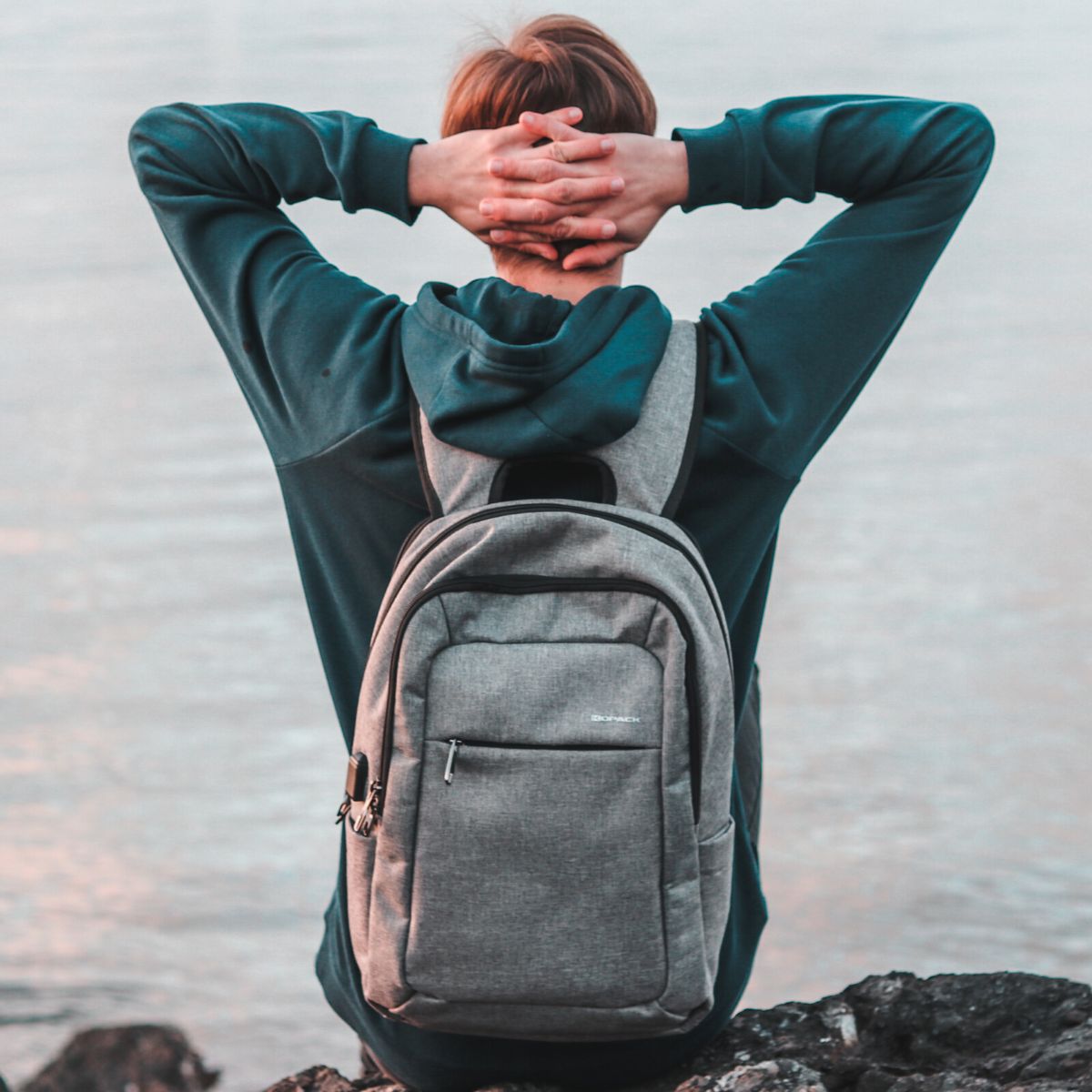 A boy with his hands folded behind his head wears a backpack.