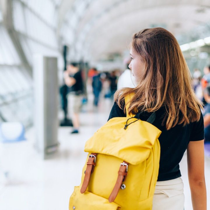 A girl walks through an airport with a yellow backpack.