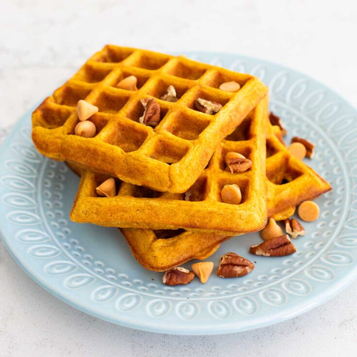 A blue plate has a stack of pumpkin pecan waffles with butterscotch chips sprinkled over the top.