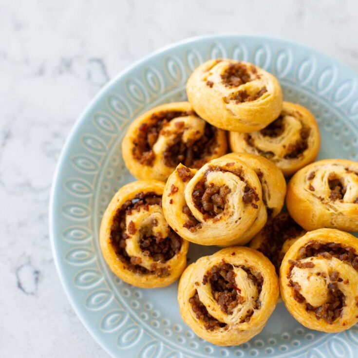 A blue plate has several savory sausage pinwheels on top.