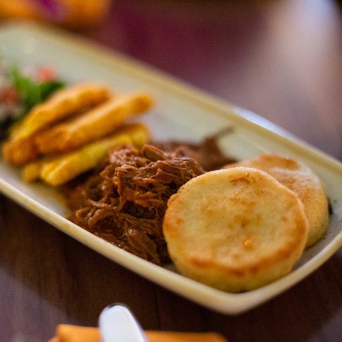 A plate of pulled pork next to corn cakes.