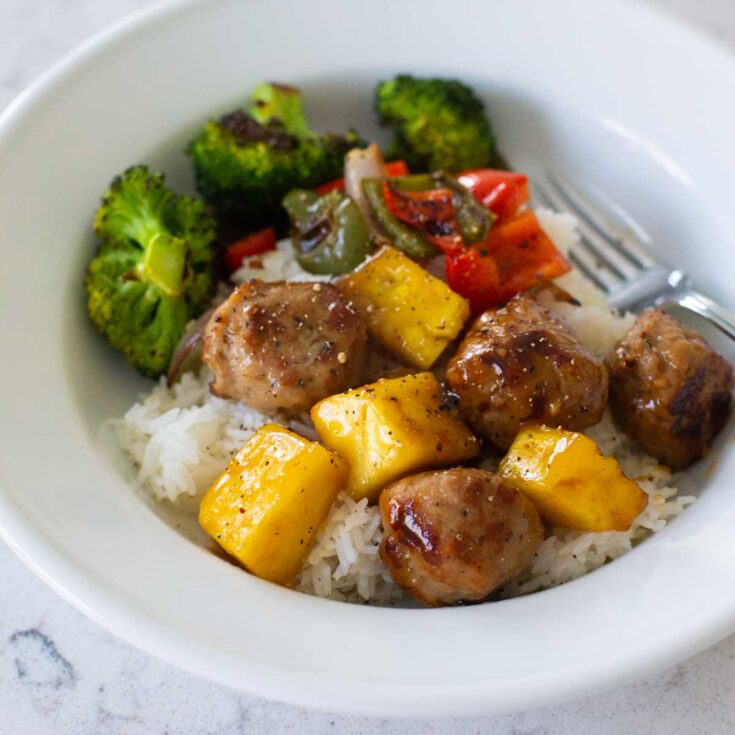 A bowl of meatballs with rice, pineapple, and broccoli.