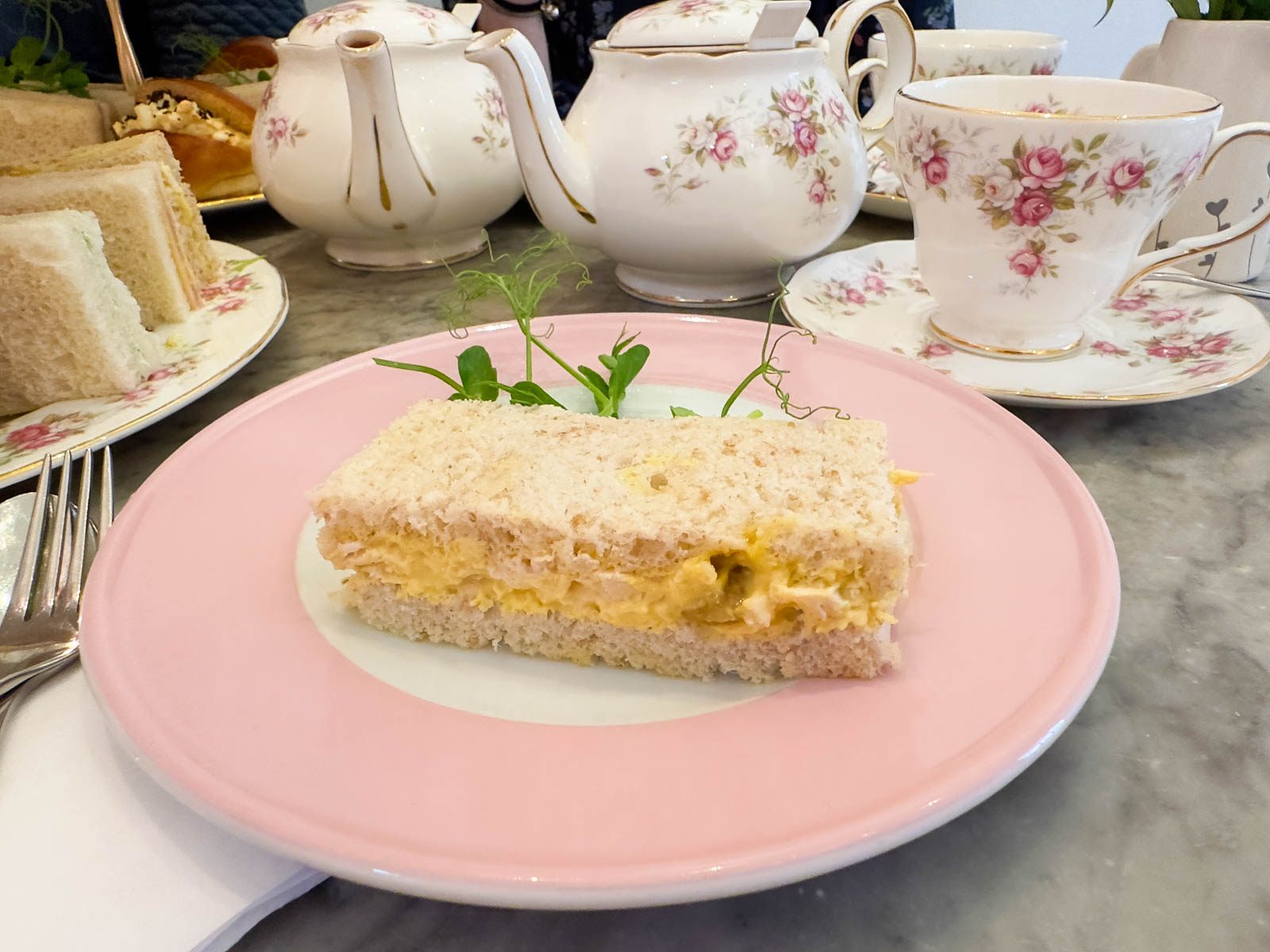 A coronation chicken salad sandwich on a pink tea plate at a tea shop in London.