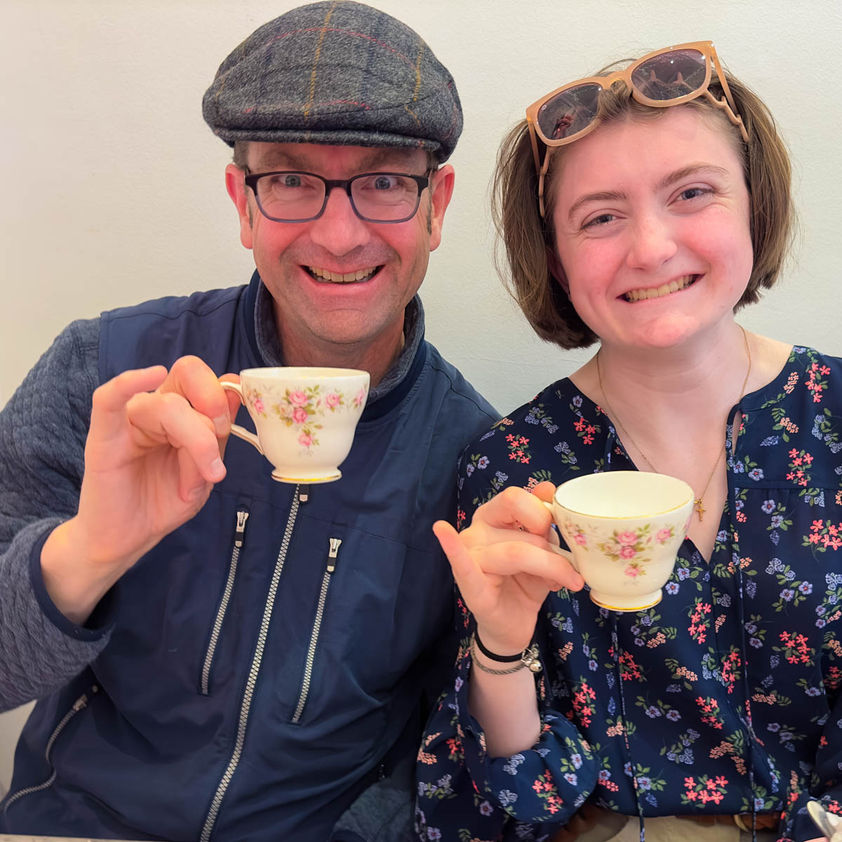 A dad and his daughter drink tea by holding their tea cups with their pinkies up.