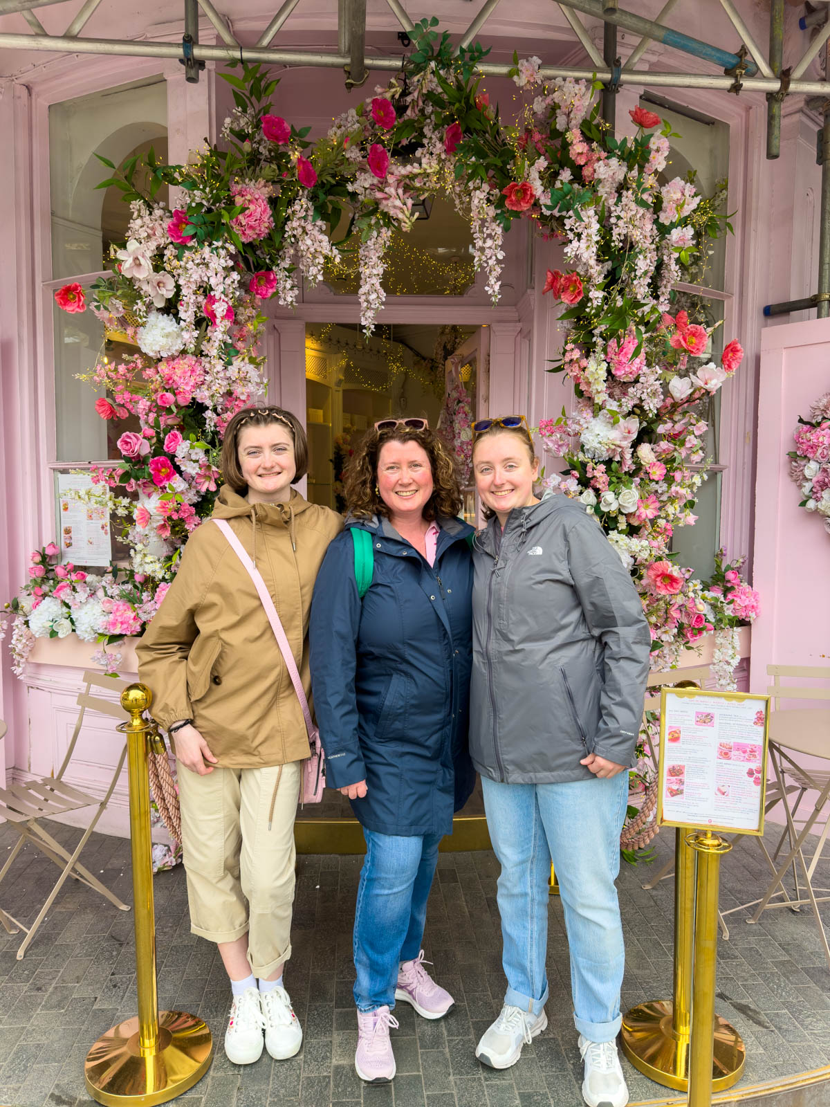 A mom and her daughters stand under the floral arch outside Peggy Porschen's in London.