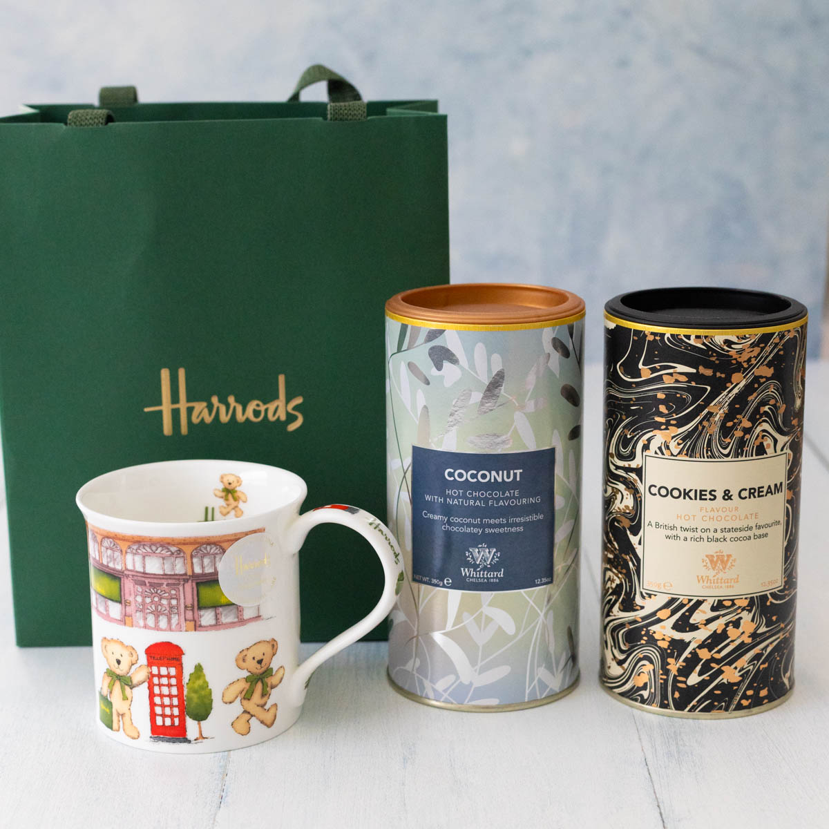 2 canisters of hot cocoa with a fancy mug and a Harrods shopping bag.