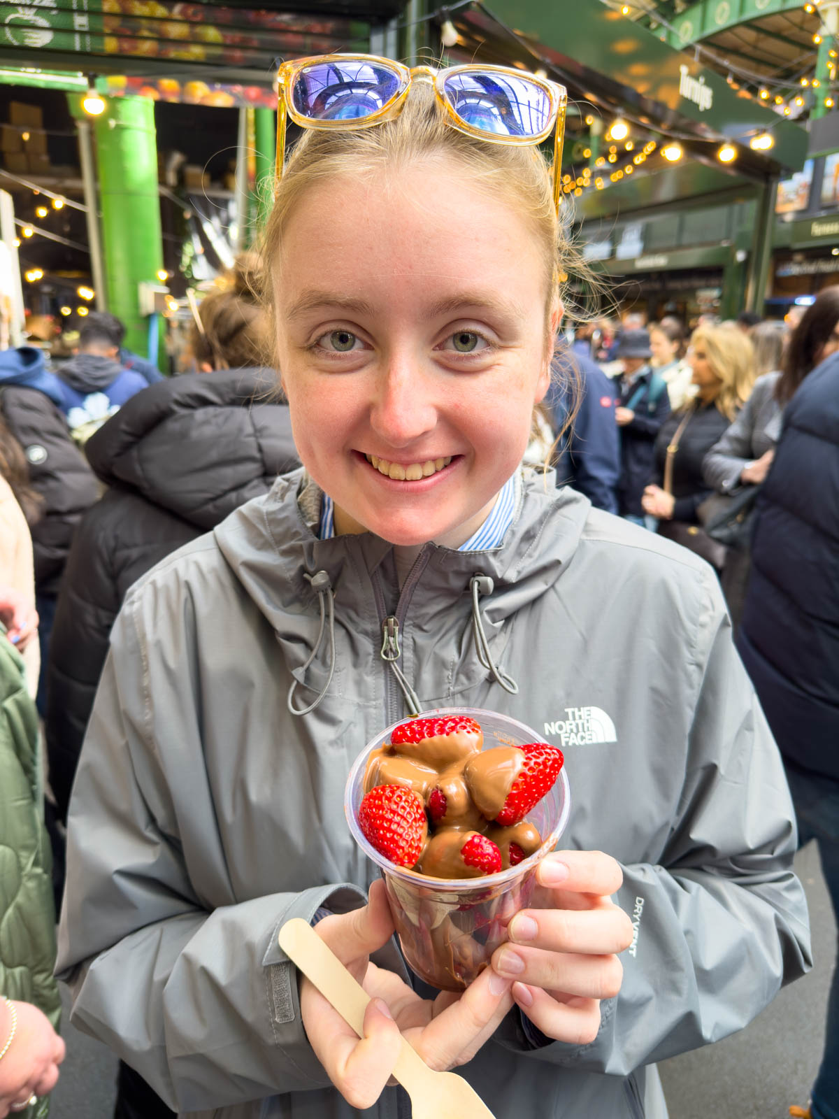 A teen girl holds a cup of fresh strawberries covered in melted chocolate.