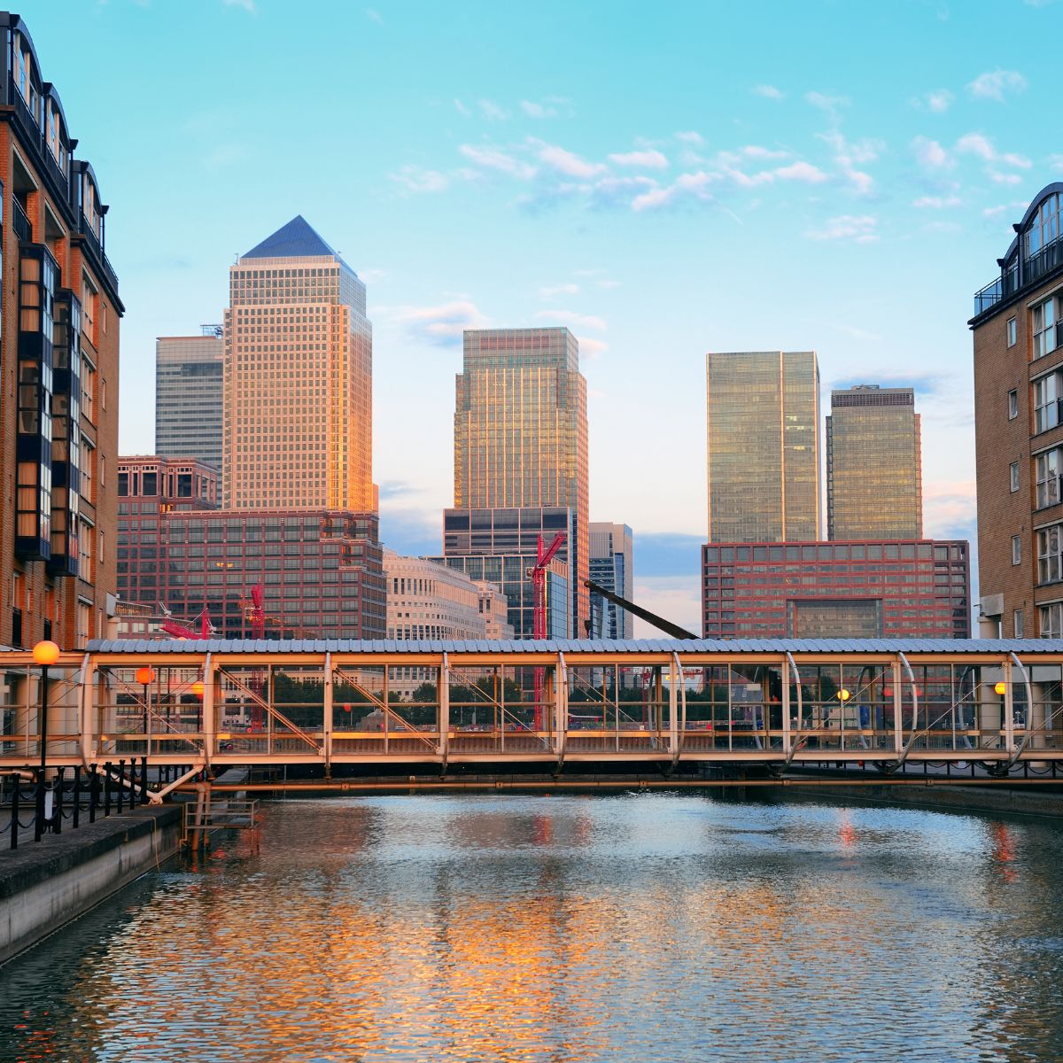 A view of Canary Wharf with a bridge over the water and tall buildings in the background.