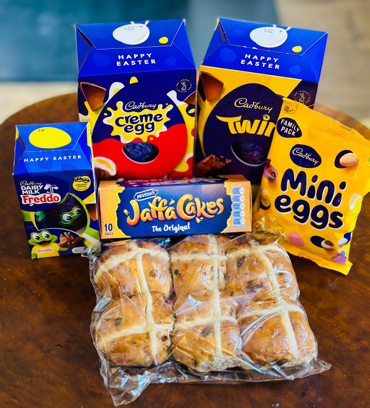 The Cadbury Easter candies sit on a table next to a package of hot cross buns.