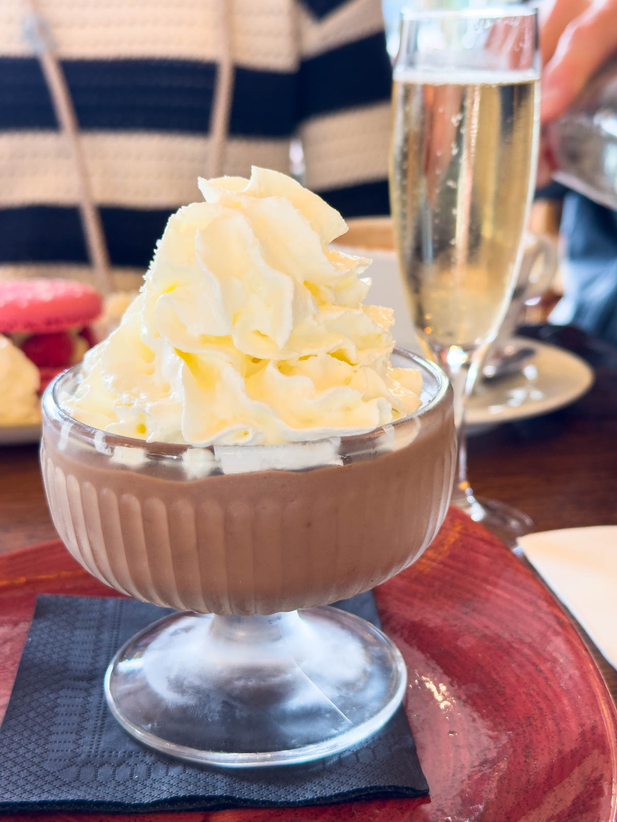 A dish filled with chocolate mousse has a giant swirl of whipped cream on top and a glass of champagne in the back.