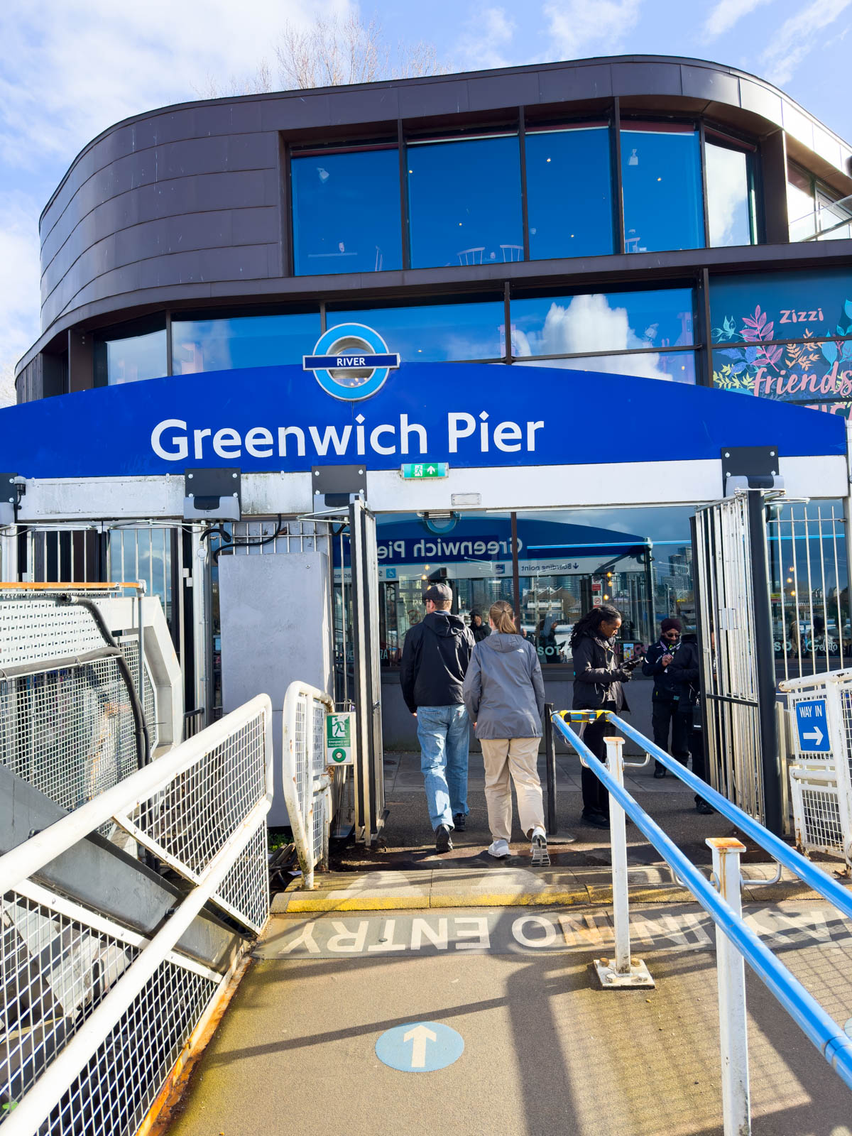 A father and daughter are walking up the pier towards the "Greenwich Pier" sign.