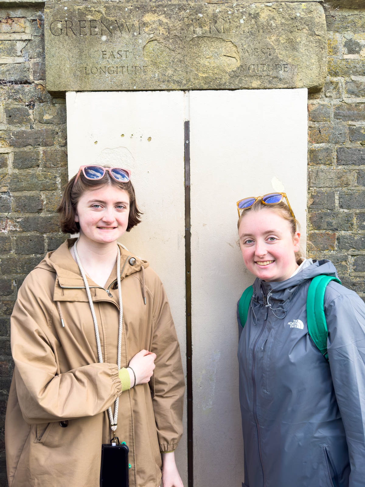 Two sisters stand on either side of the prime meridian line in Greenwich.