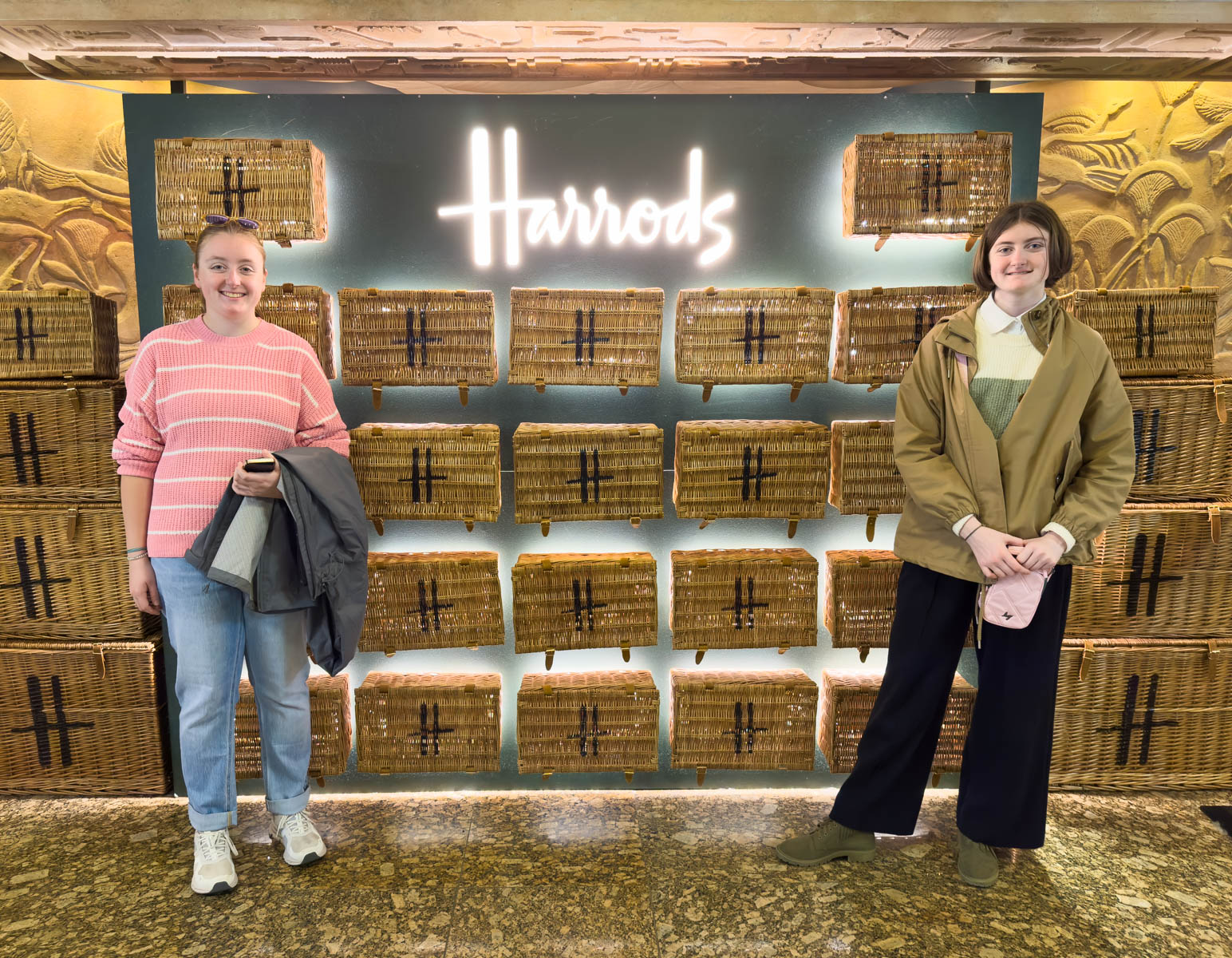 Two girls stand in front of the Harrods sign.