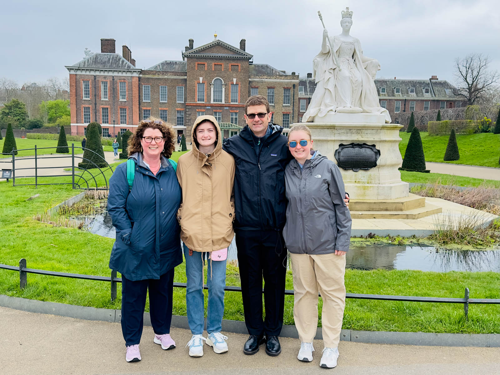 A family of four stands out front of Kensington Palace near the Queen Victoria statue.