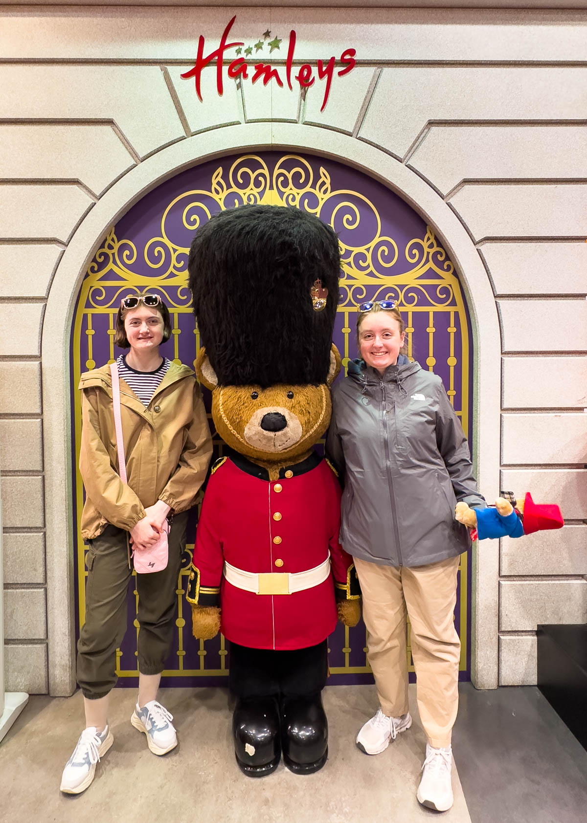 Two young girls stand with a toy bear dressed like a London guard.