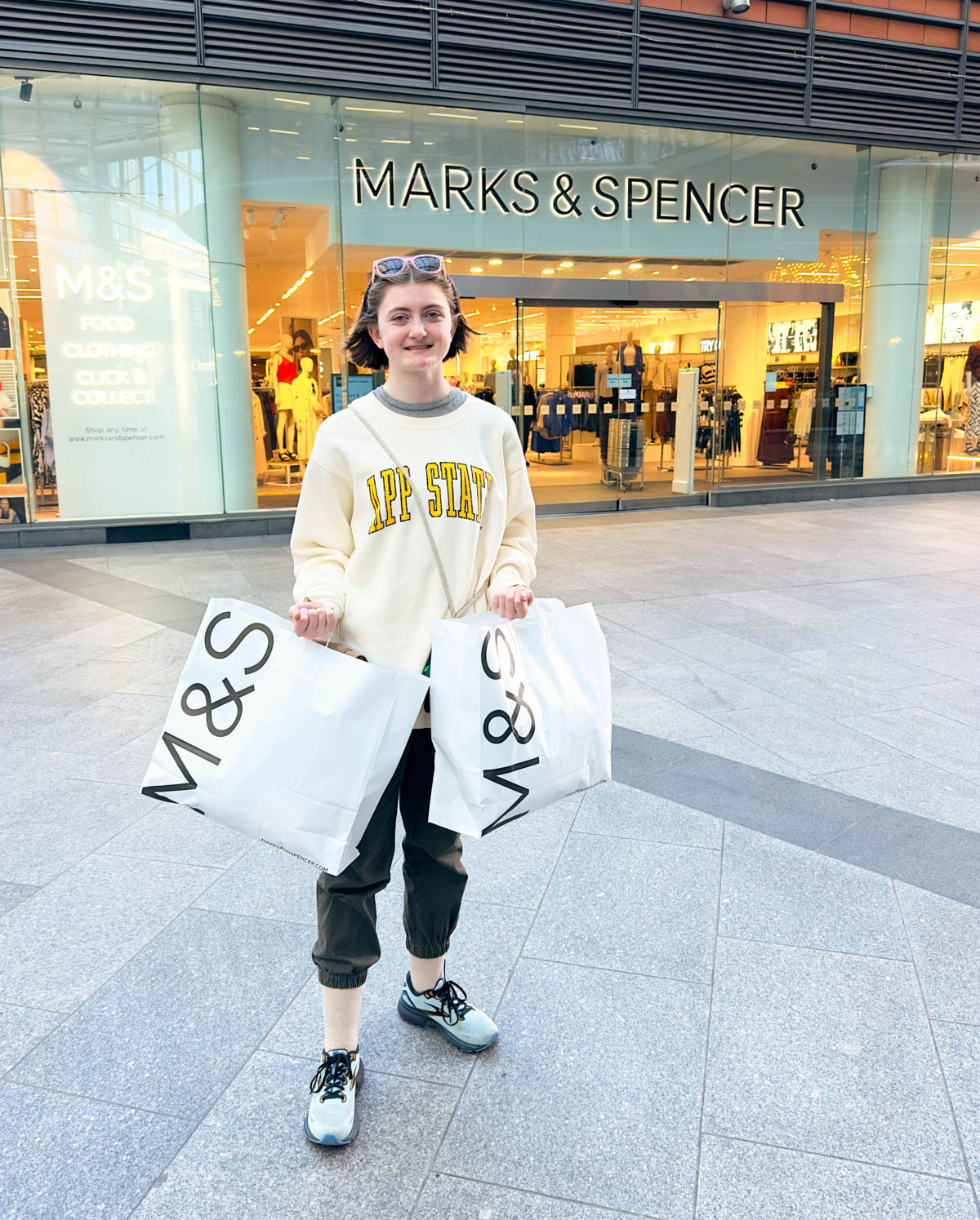 A young girl holds shopping bags in front of Marks & Spencer.
