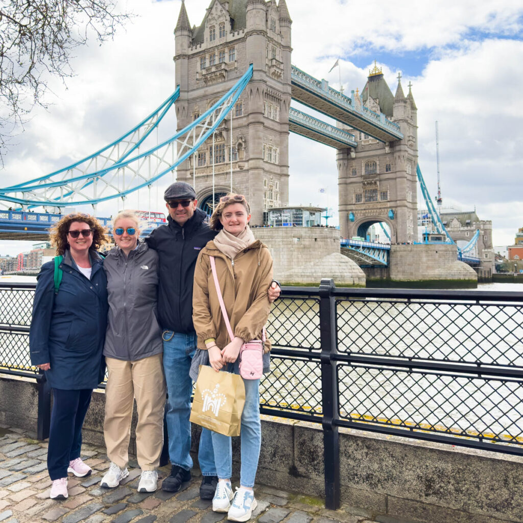 A family of four stands in front of the Tower Bridge in London.