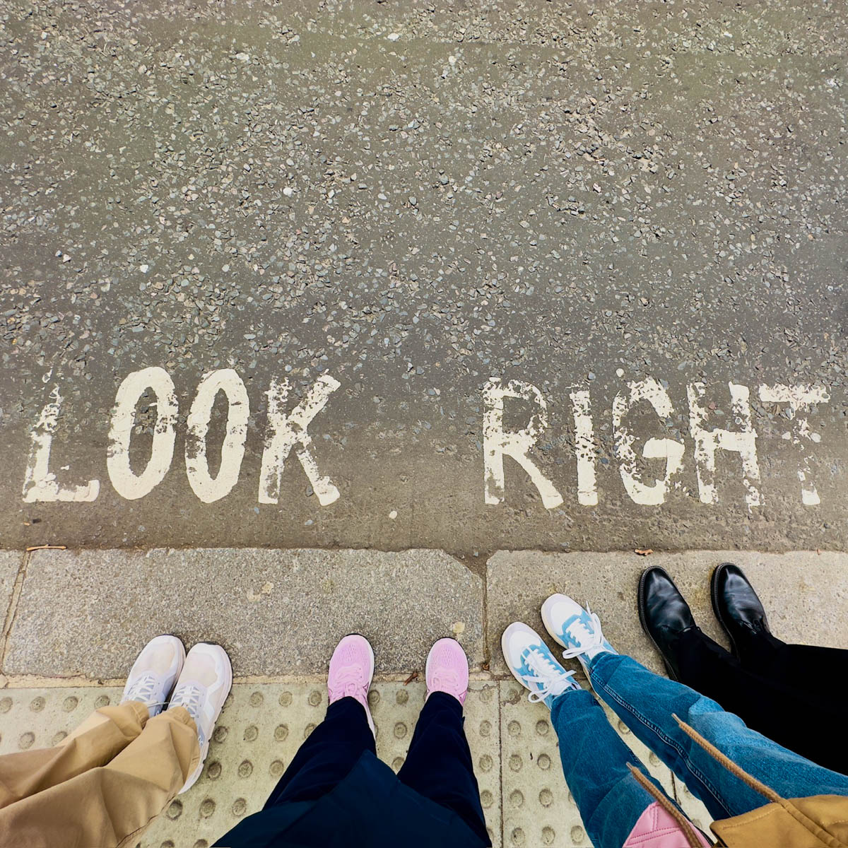 The street has been painted with the message "Look Right". Four pairs of feet are lined up at the sidewalk ready to cross.