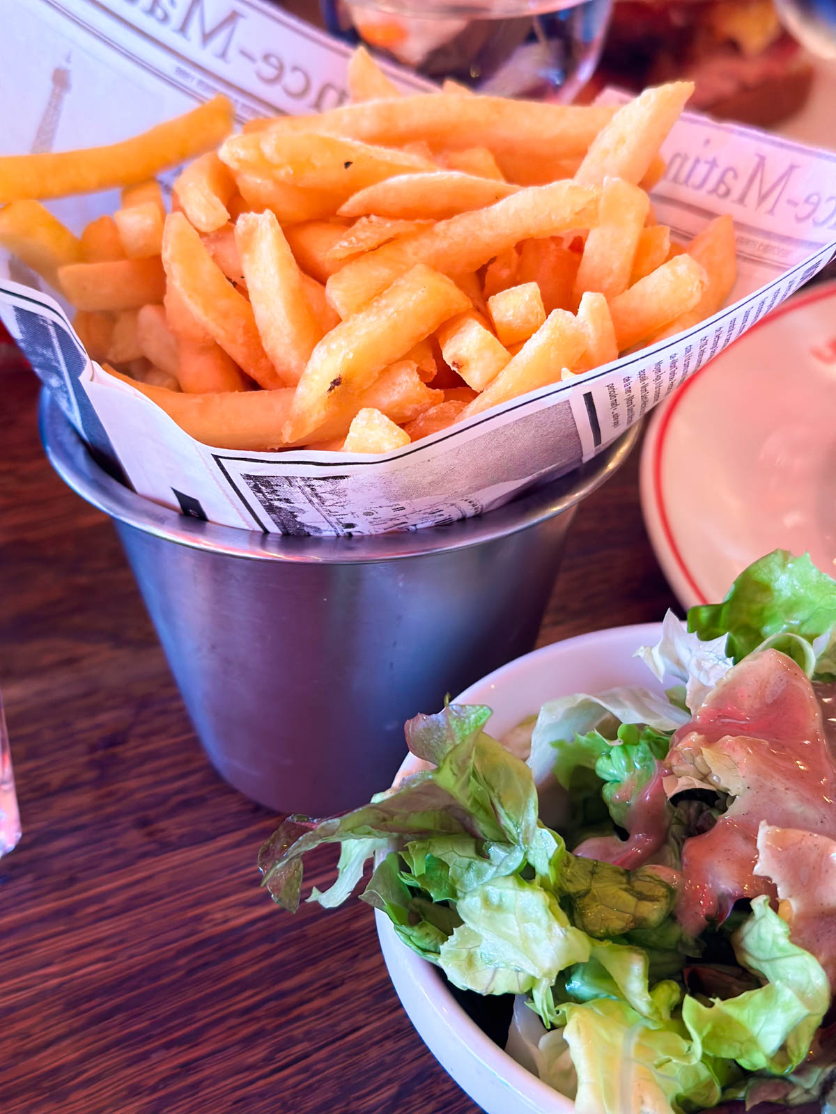 A container of french fries sits next to a small salad.