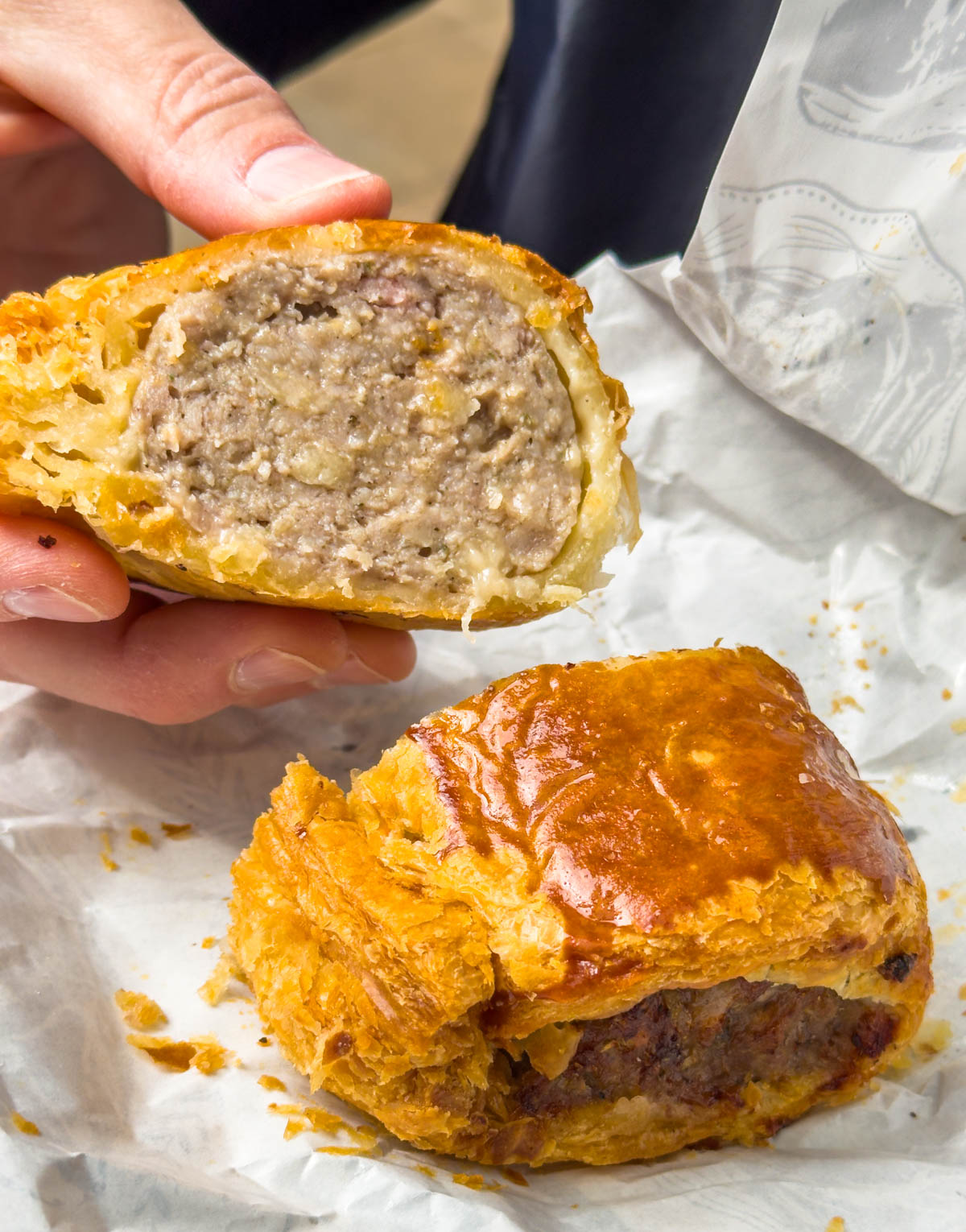 A sausage roll has been cut in half and is being held up to show the filling.