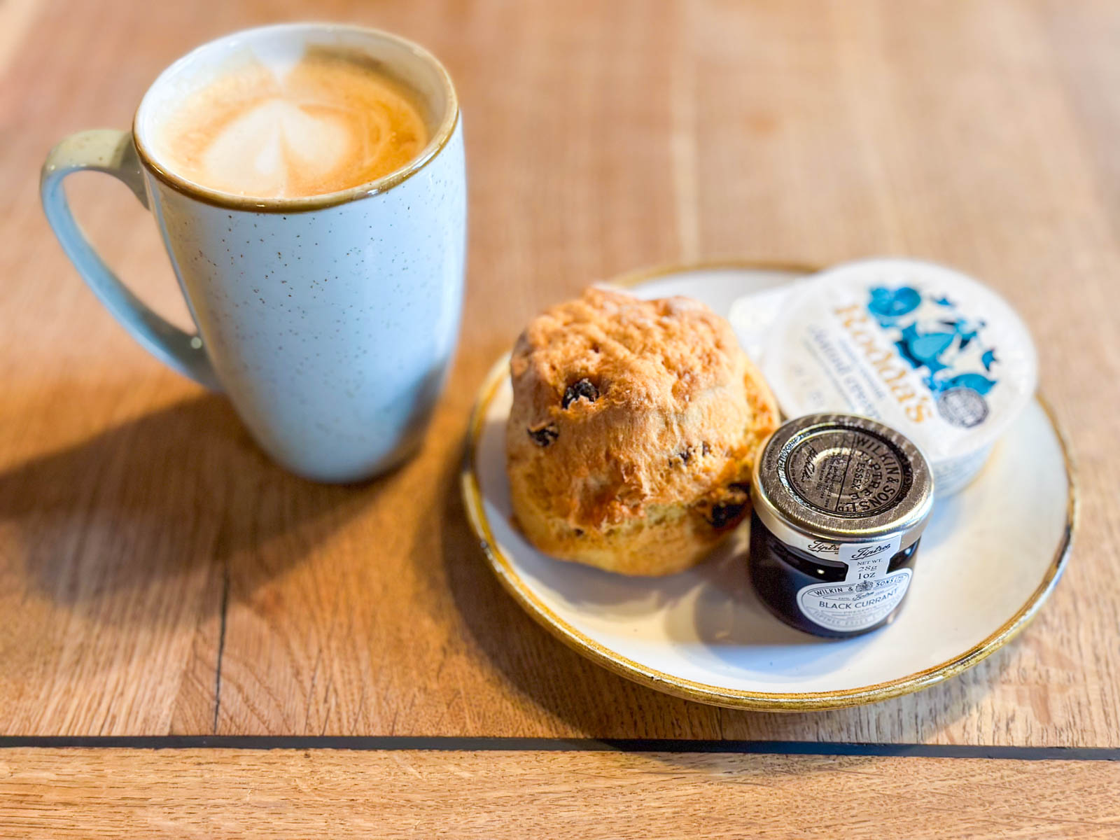 A plate with a scone, jam, and clotted cream sits next to a mug of coffee.