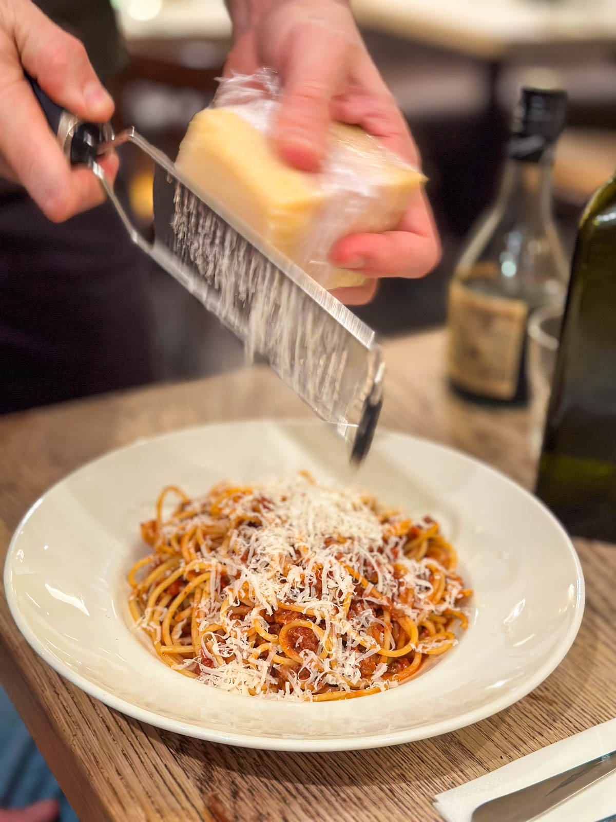 A hand is grating parmesan over a bowl of spaghetti.