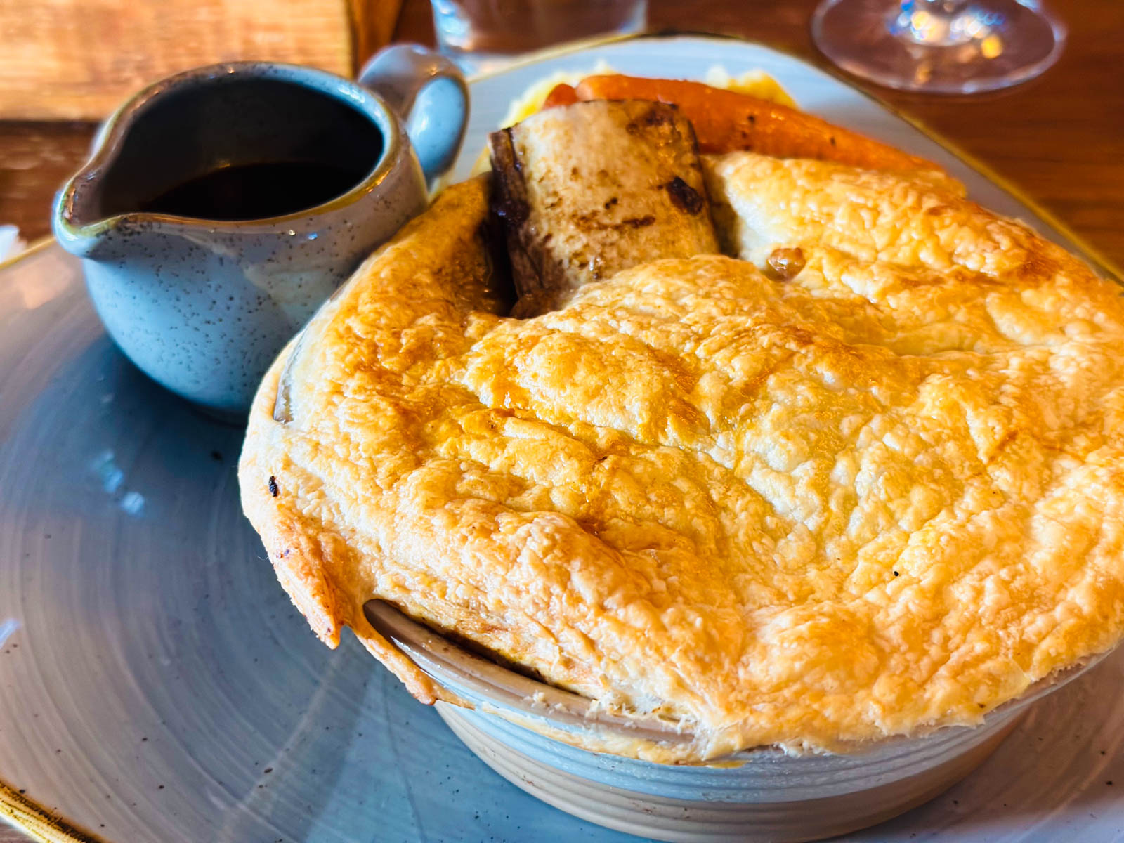 A pastry topped beef pie has a bone sticking out of the top and a pitcher of gravy on the side.