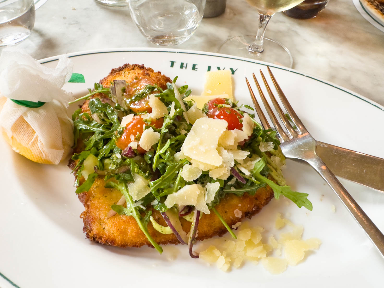 A breaded chicken cutlet is topped with rocket, parmesan, and tomatoes.