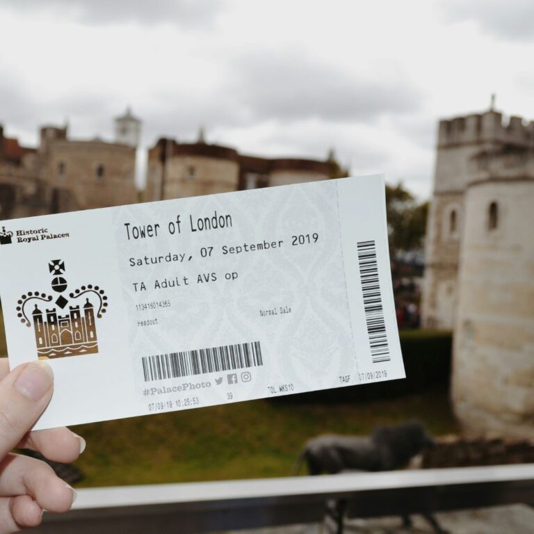 A paper ticket for the Tower of London is being held up in front of the Tower of London itself.