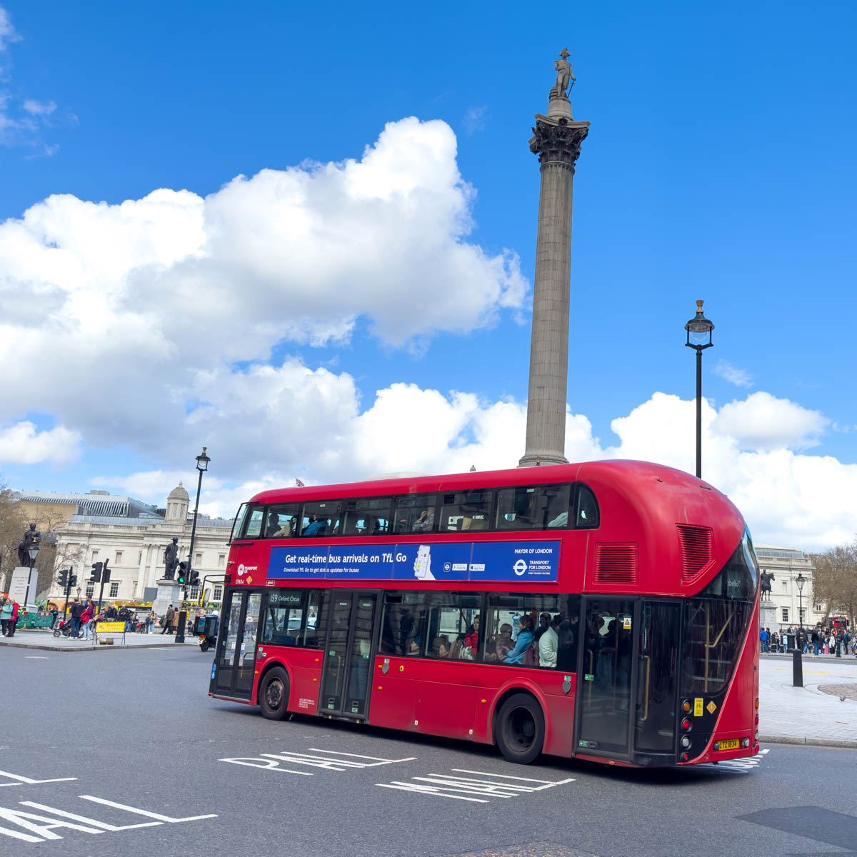 A red bus is driving past the Lord Nelson statue in London.