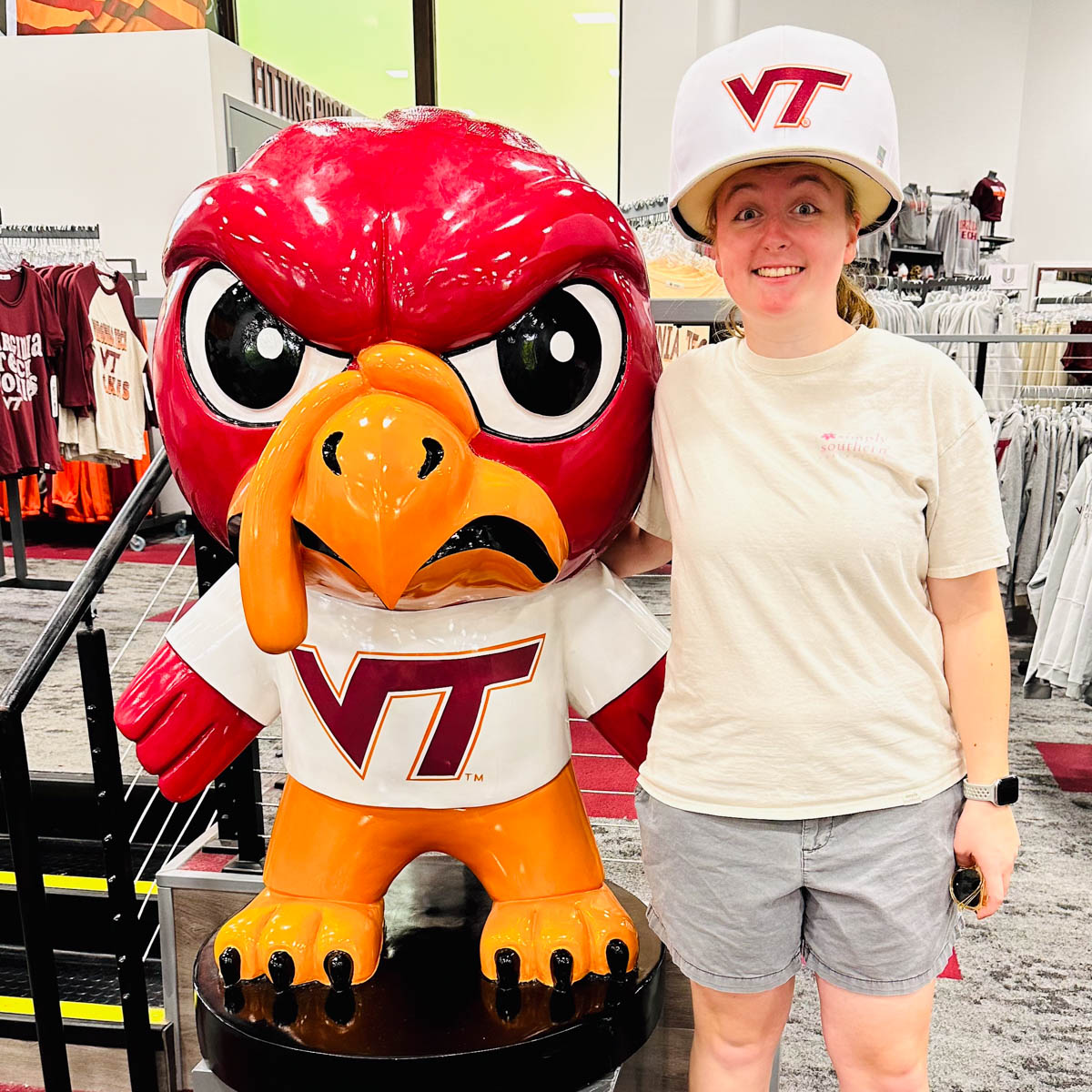A prospective student visits the VT university book store and stands next to a statue of the Hokie bird mascot.