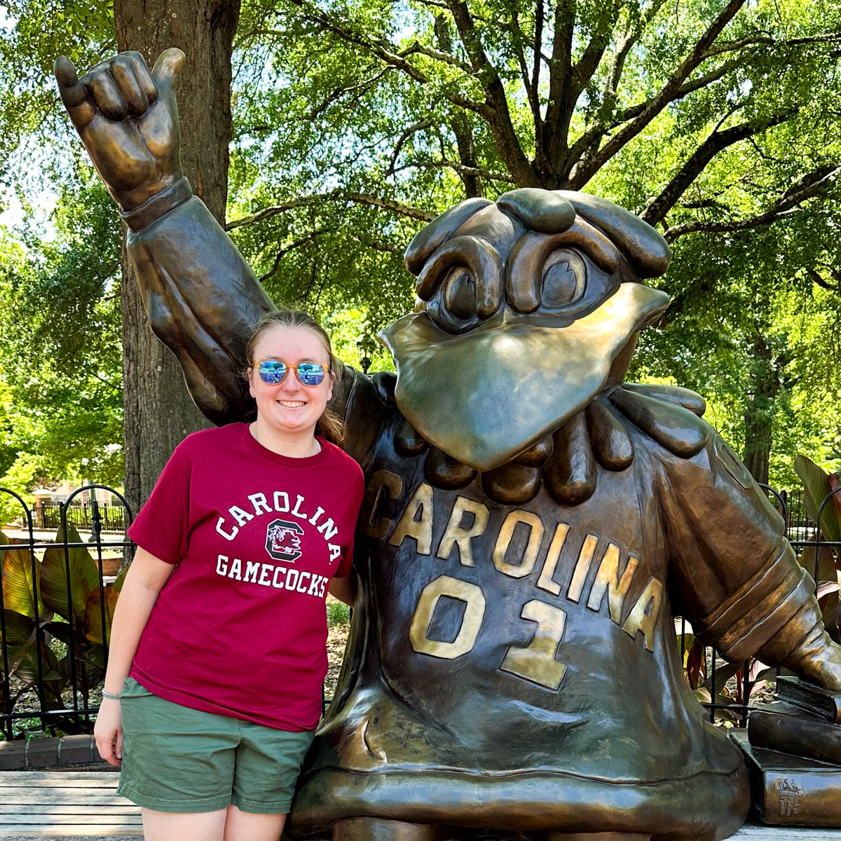 A girl in a Gamecock t-shirt stands next to the statue of the University of South Carolina mascot.