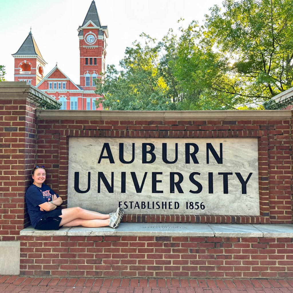 A girl sits in front of the Auburn University sign.