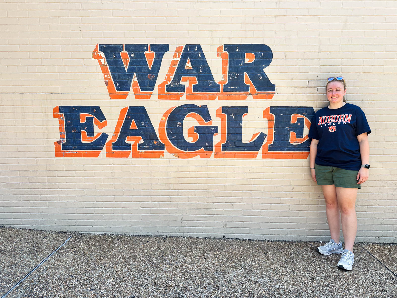 A girl stands in front of a wall painted to say "War Eagle"