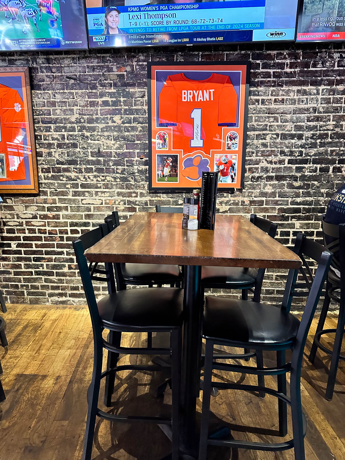 The inside of the sports pub has a table and chairs with a Clemson jersey framed on the wall behind.