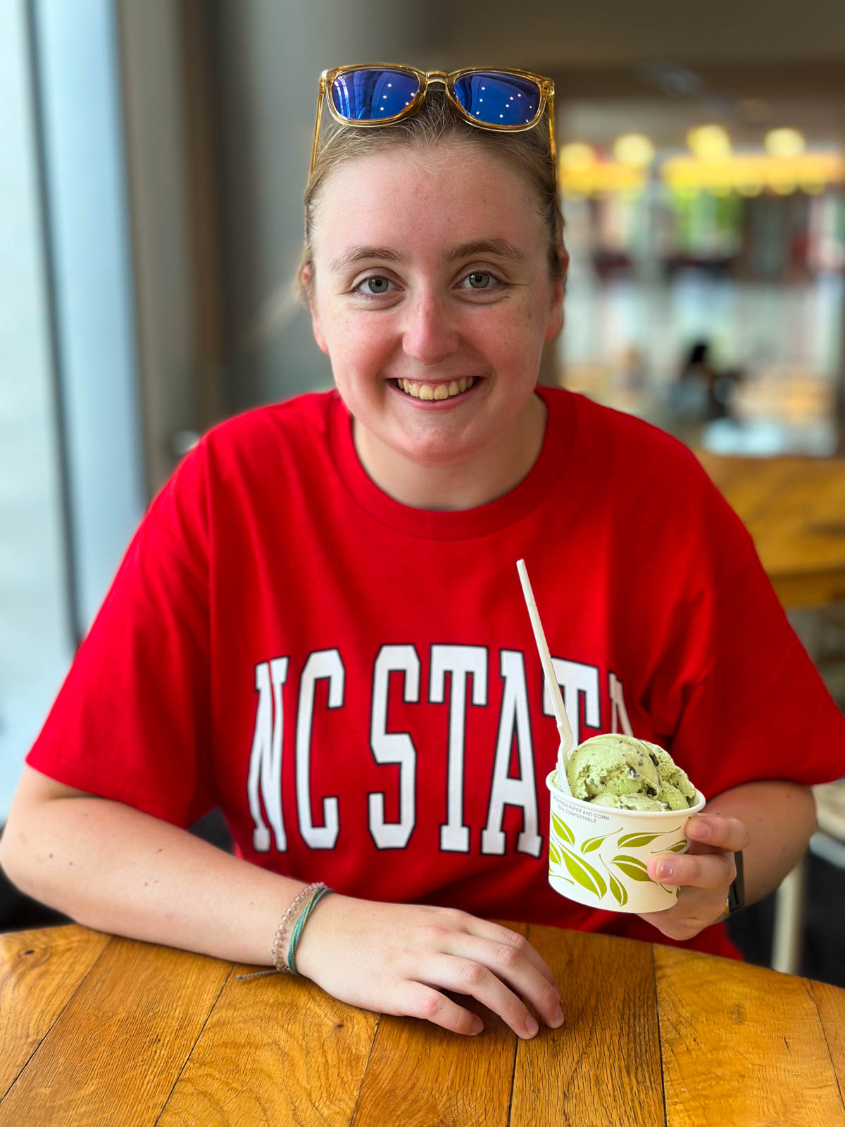 A girl wearing a red NC State t-shirt eats ice cream in the student union.