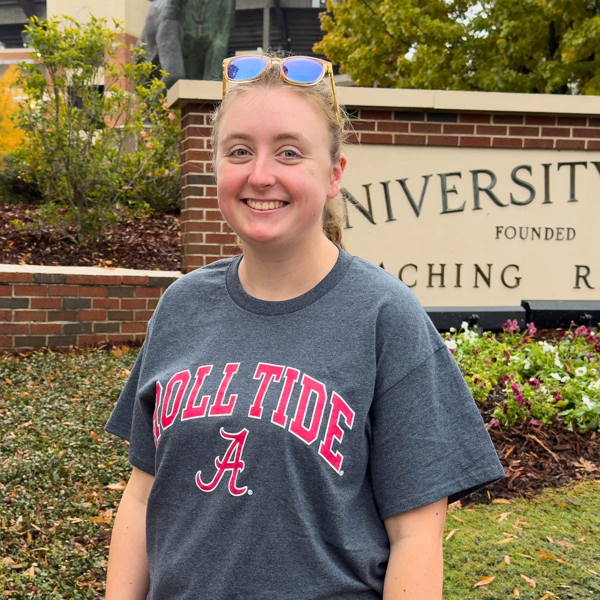 A girl wears a Roll Tide t-shirt in front of the University of Alabama sign.